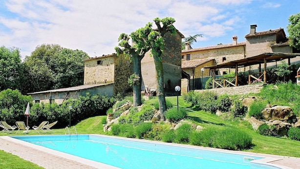 A swimming pool with a stone border, surrounded by lush greenery and a stone building with a tiled roof. - Modern Holiday Home in Monte Santa Maria Tiberina (Monte Santa Maria Tiberina)