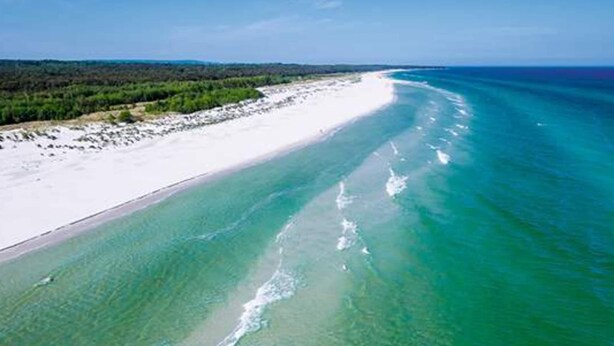 Vue aérienne d’une plage aux eaux turquoise et au sable blanc.