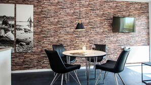 Un espace repas moderne avec un mur en pierre, des chaises noires, une table ronde et un luminaire suspendu.