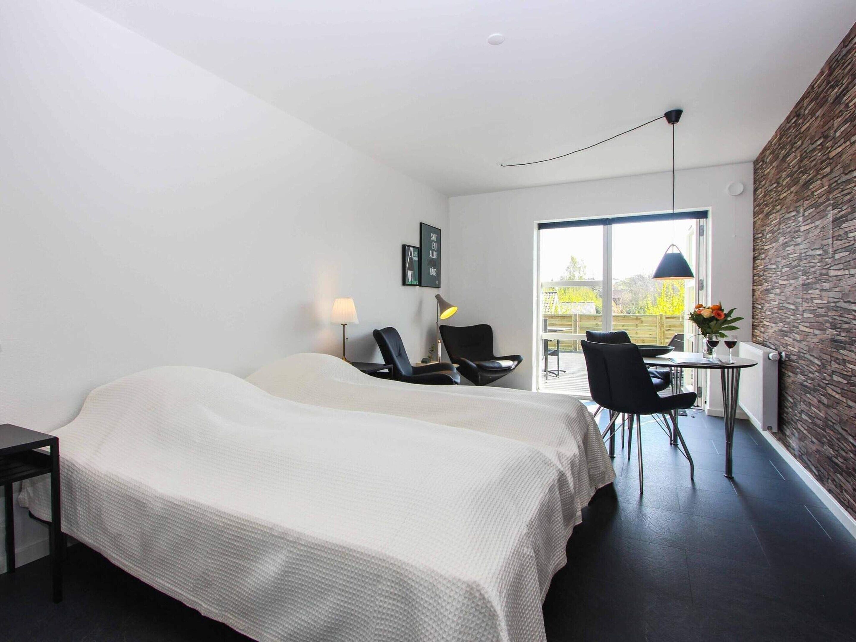 A modern hotel room with a large bed, two chairs, a small table, and a view of the outdoors.
