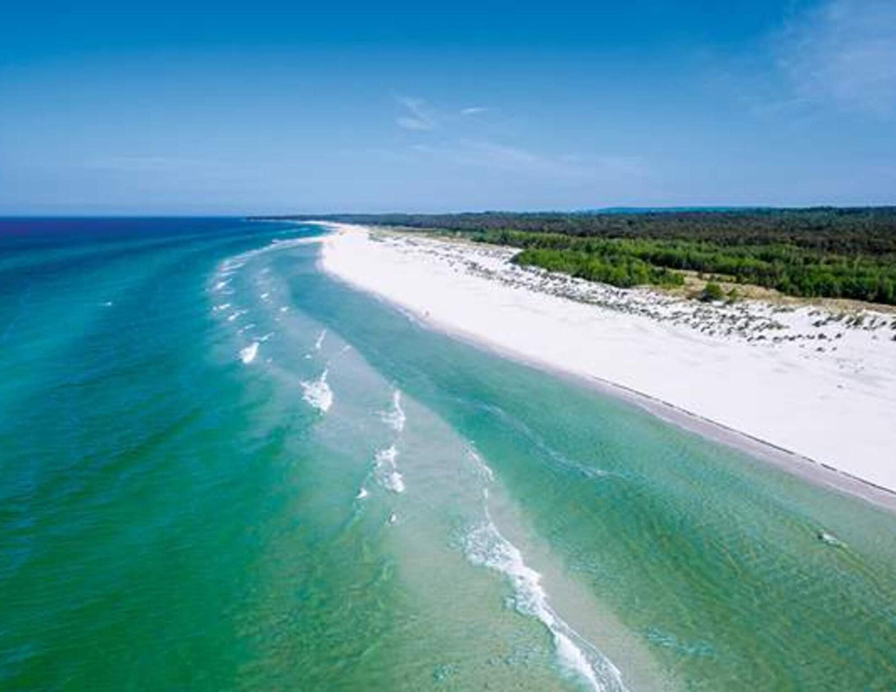 An aerial view of a beach with clear turquoise waters and white sand.