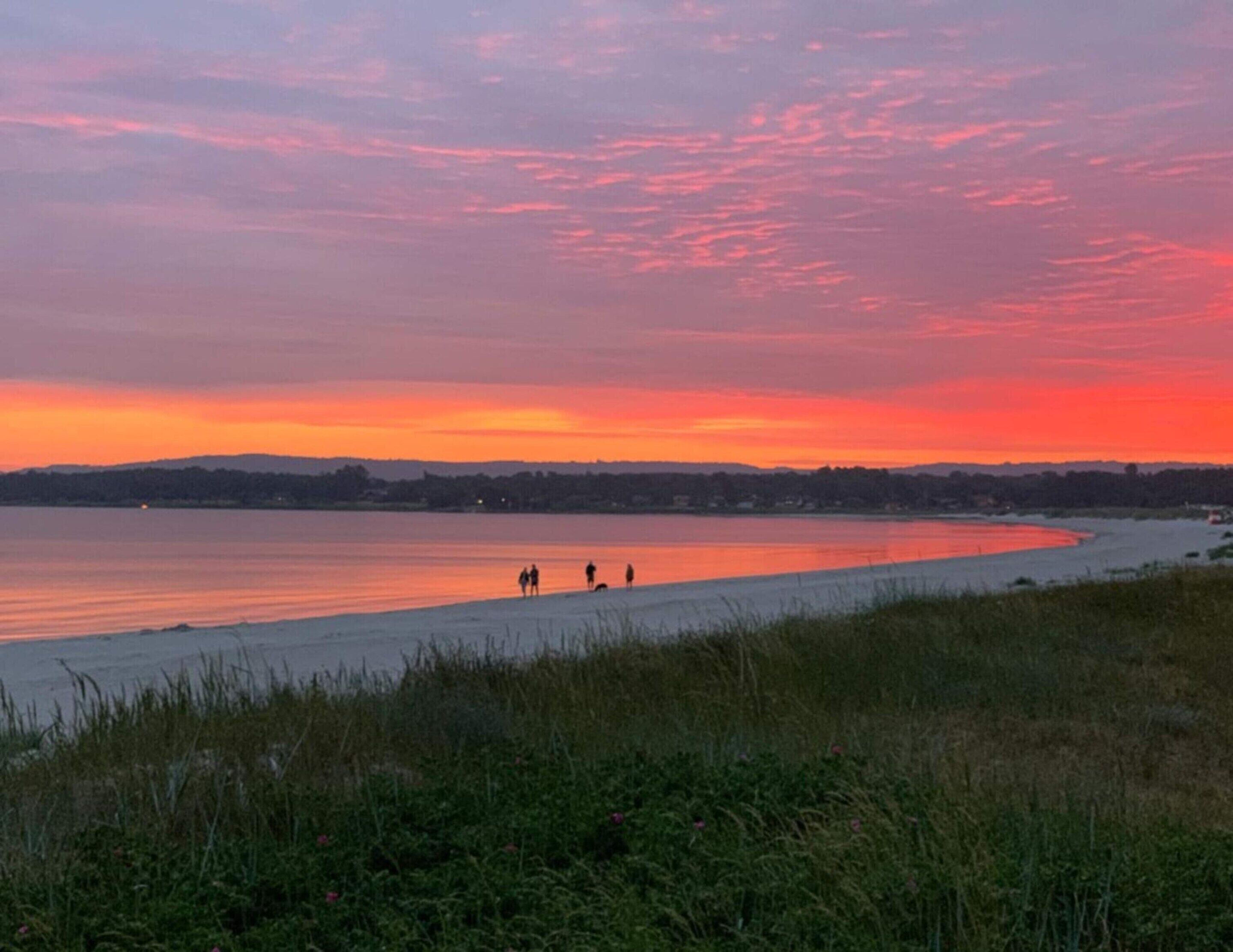 Ein Strand bei Sonnenuntergang, ruhiges Wasser und einige Spaziergänger.