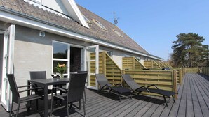 Une terrasse avec une table et des chaises, une clôture en bois et un bâtiment doté d’un toit en pente.