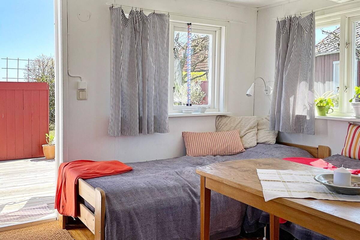 Ein gemütliches Zimmer mit zwei Betten, einem Holztisch und einem Fenster mit gestreifter Gardine.