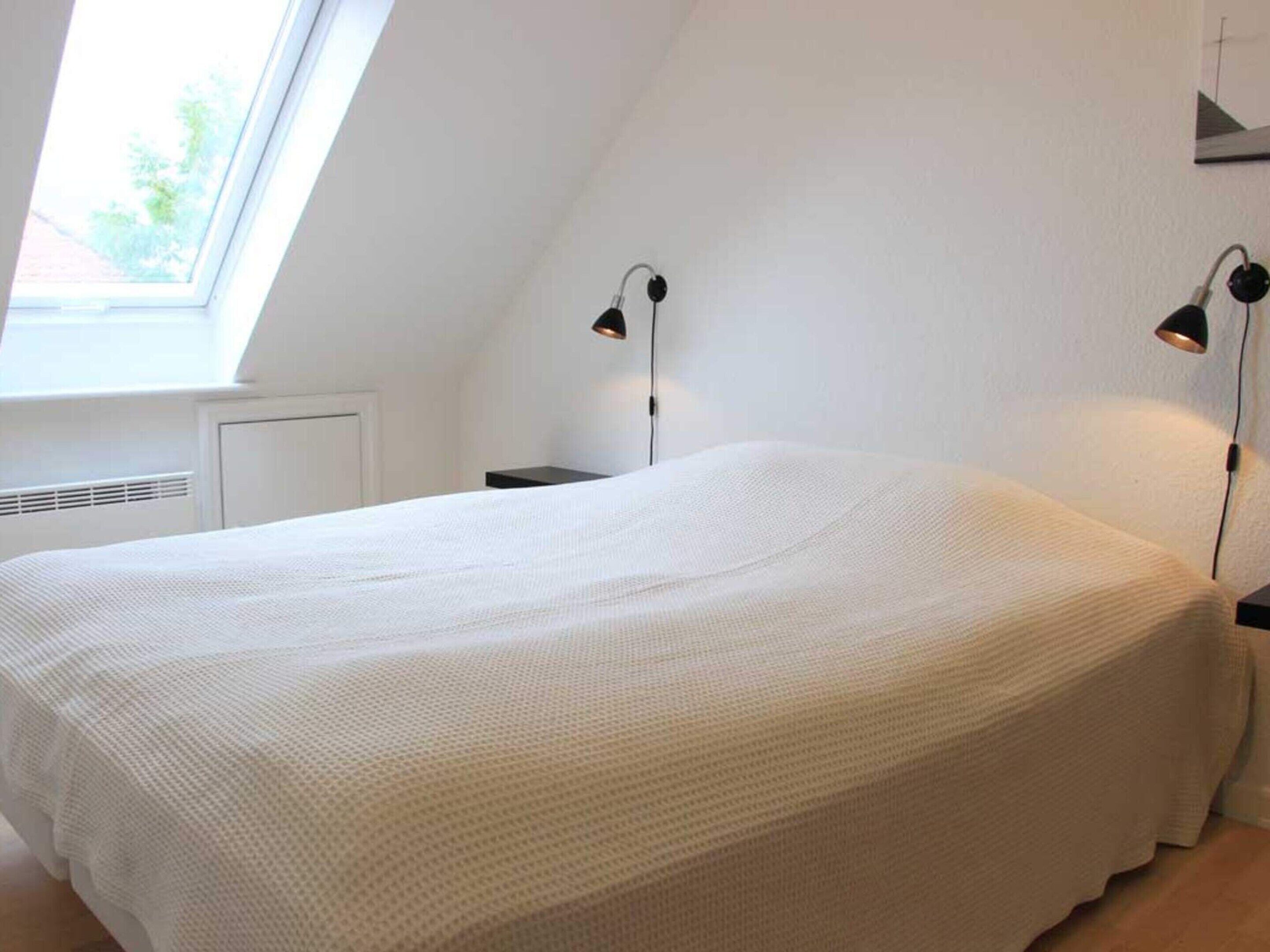 Une chambre avec un grand lit, deux lampes de chevet, une fenêtre et un radiateur.