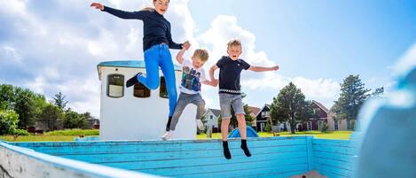 A child and an adult jumping on a blue play structure in a park.