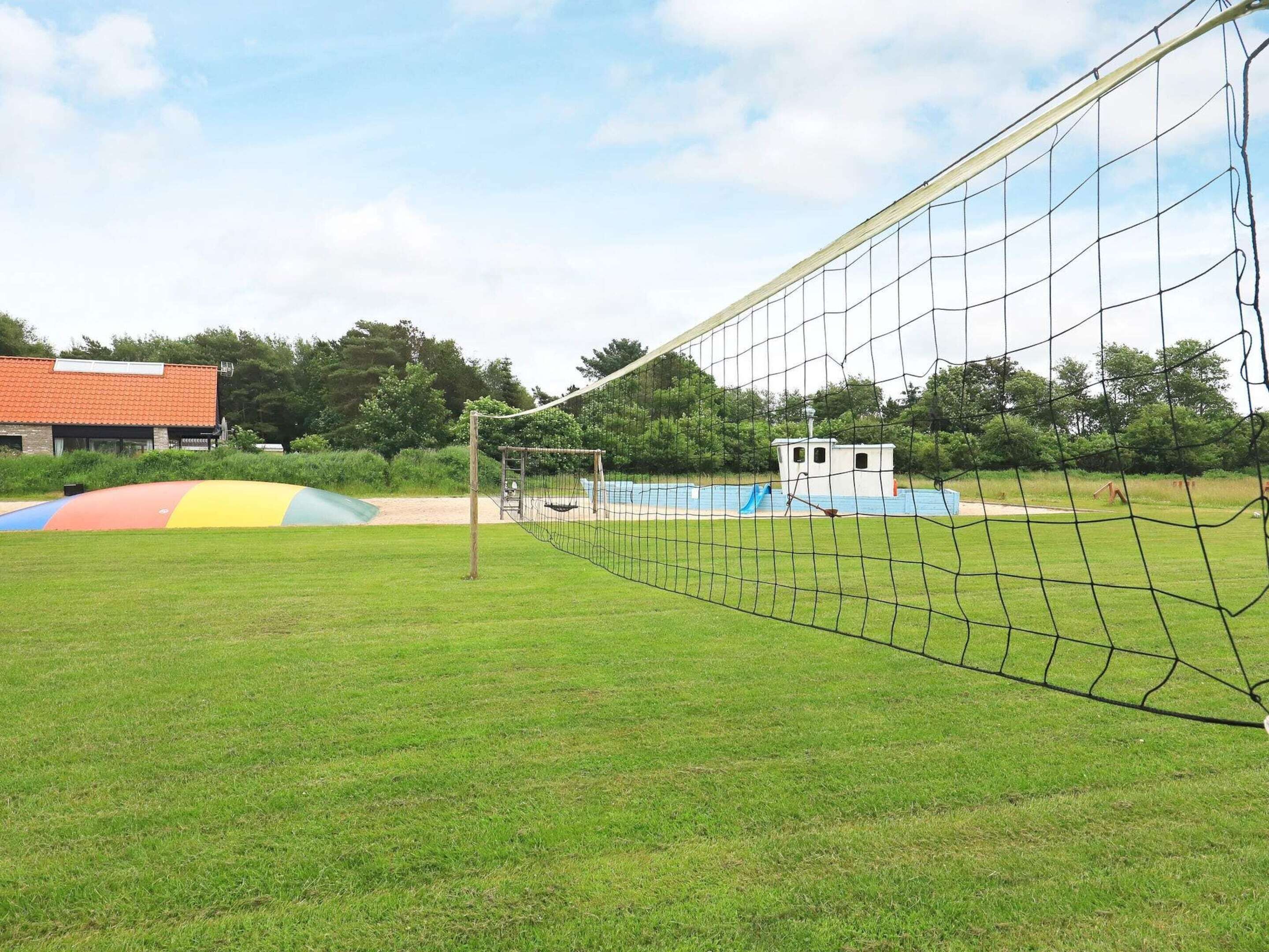 Een sportveld met een doelpaal met net, een klein gebouw en een kleurrijke speelconstructie.