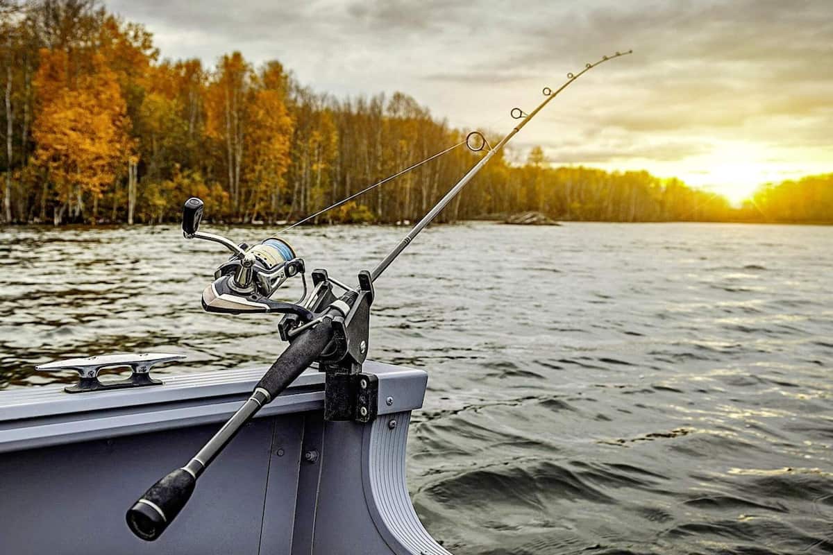 A fishing rod mounted on a boat with a forest and sunset in the background.