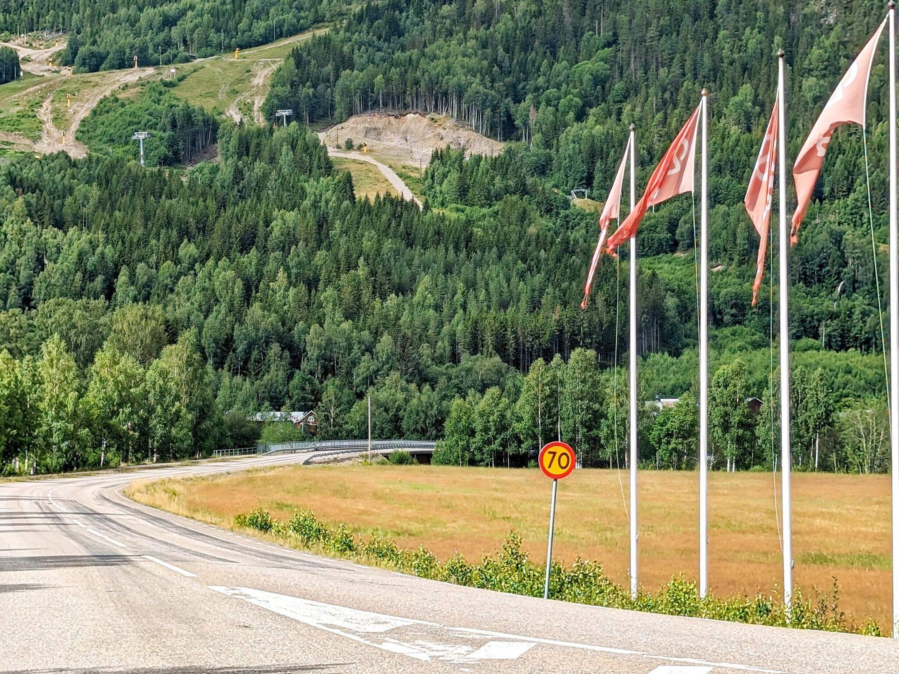 Een kronkelende weg met een snelheidslimiet bord van 70, omringd door weelderige begroeiing en een beboste heuvel.