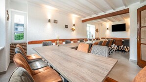 A conference room with a long table, cushioned chairs, and a television mounted on the wall. - Grosse Gruppenunterkunft im Nationalpark Eifel mit Bar und Terrasse (Schleiden)
