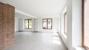 A spacious, modern interior with large windows, a brick wall, and a tiled floor. - Grosse Gruppenunterkunft im Nationalpark Eifel mit Bar und Terrasse (Schleiden)