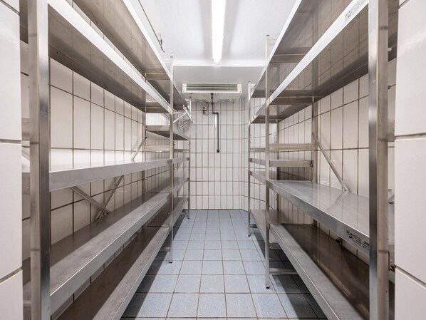 Un pasillo de hotel limpio y vacío con estanterías metálicas y paredes con azulejos.