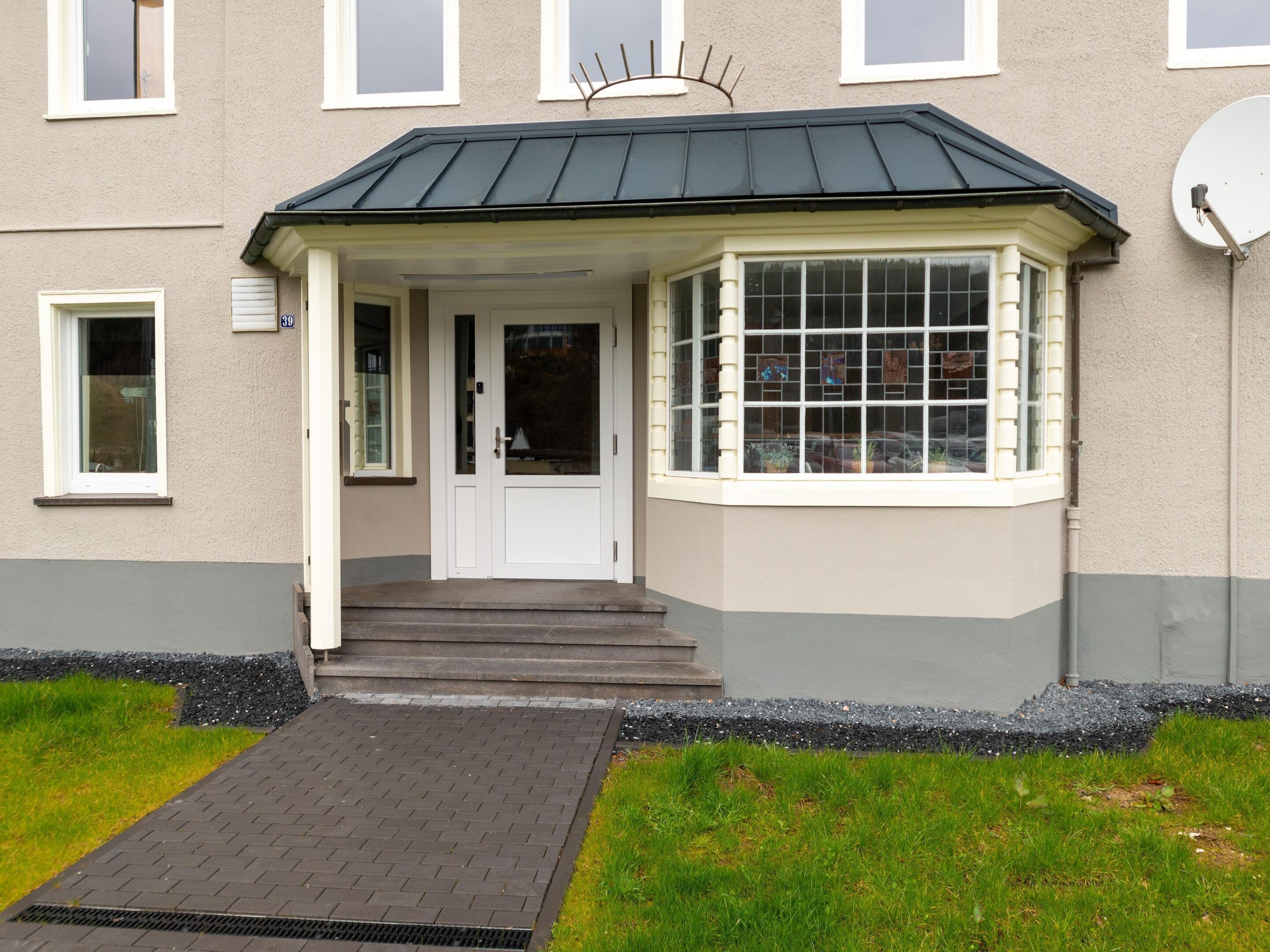 A two-story building with a front entrance, a satellite dish, and a bay window.