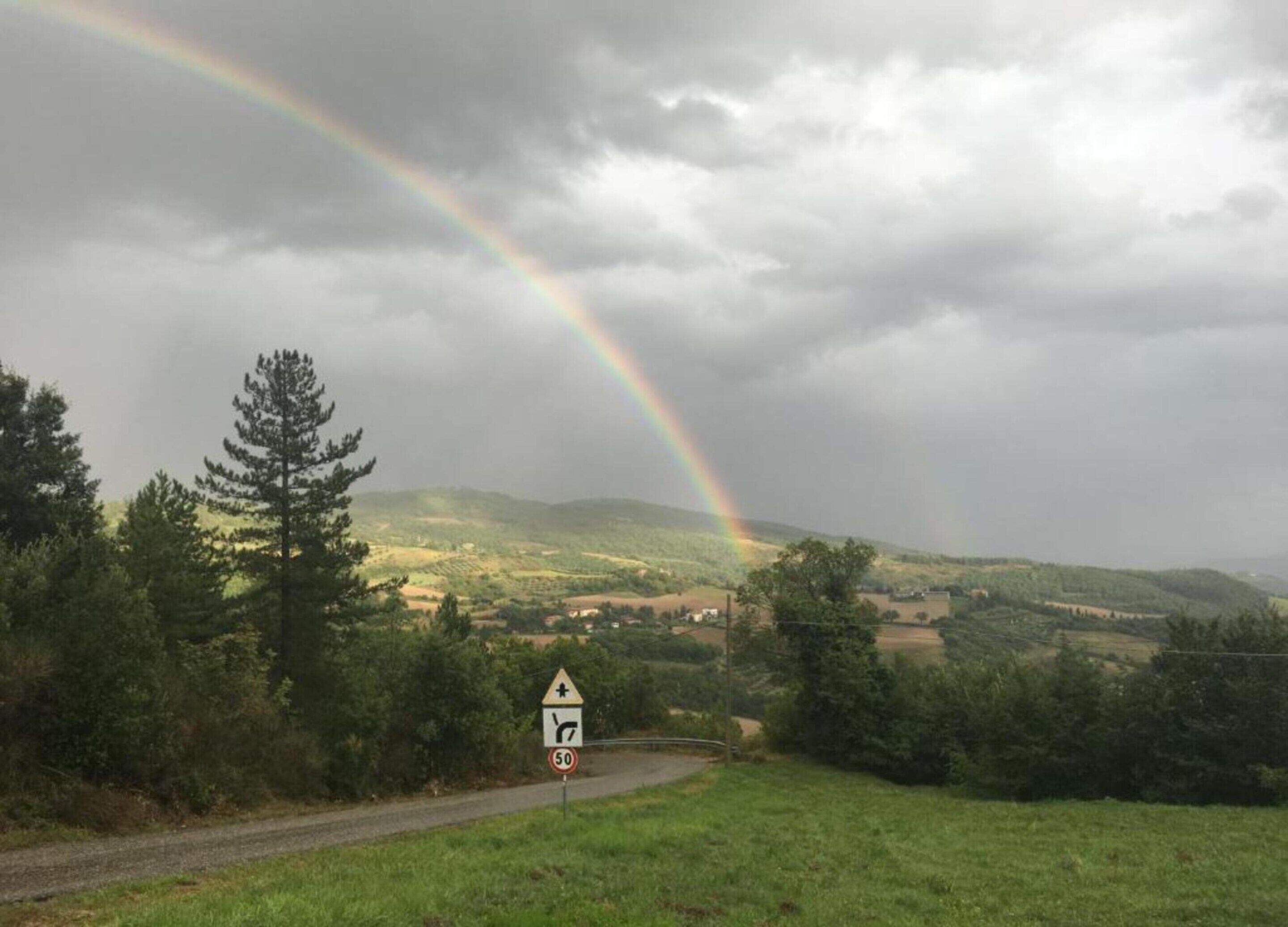 A rural landscape with a winding road, a speed limit sign, and a rainbow in the sky.