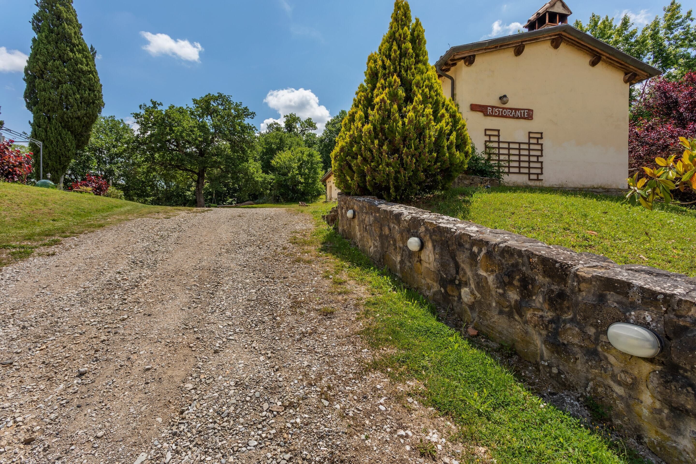 A gravel path leading to a building labeled "RISTORANTE" with a stone wall and greenery.