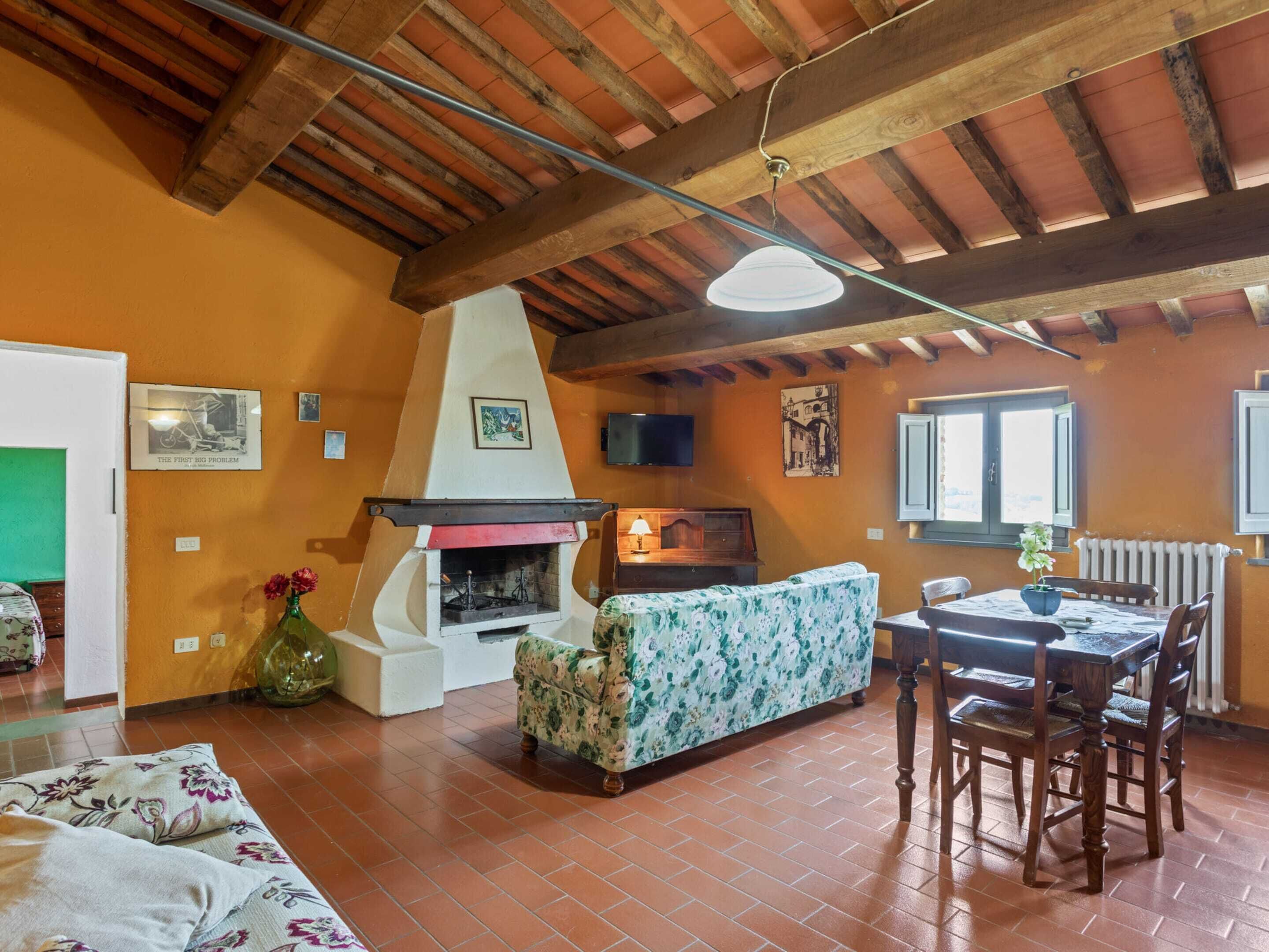 Un salón acogedor con chimenea, vigas de madera, un sofá, una mesa de comedor con sillas y un televisor.