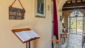 A wooden sign reading "Specialist Wine-Bar and Shop" hanging on a wall, a wooden music stand with a sheet of music, and a doorway leading to an outdoor area with tables and chairs. - Rustic Holiday Home in Citta di Castello With Swimming Pool (Città di Castello)
