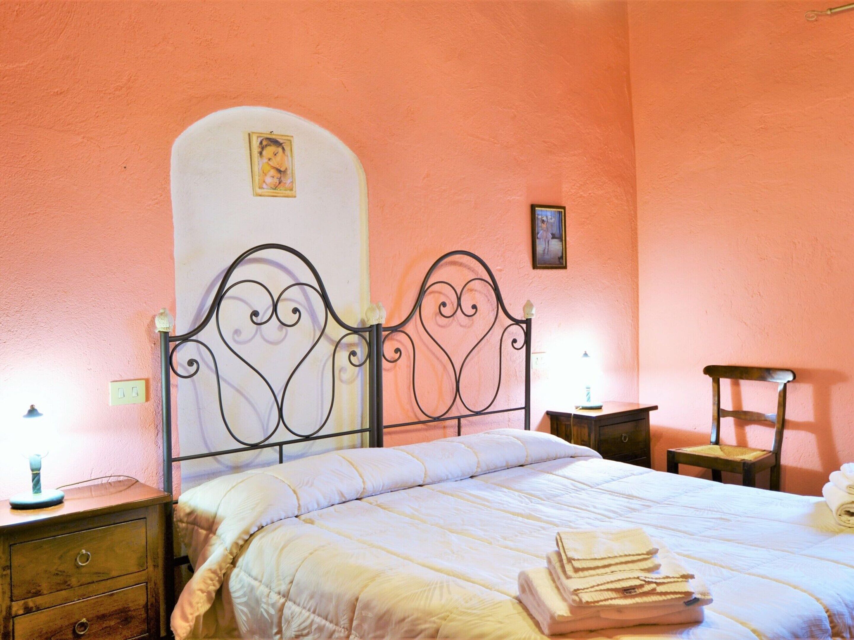 A bedroom with a bed, a nightstand, a chair, and a wall with two framed pictures.