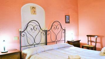 A bedroom with a bed, a nightstand, a chair, and a wall with two framed pictures.