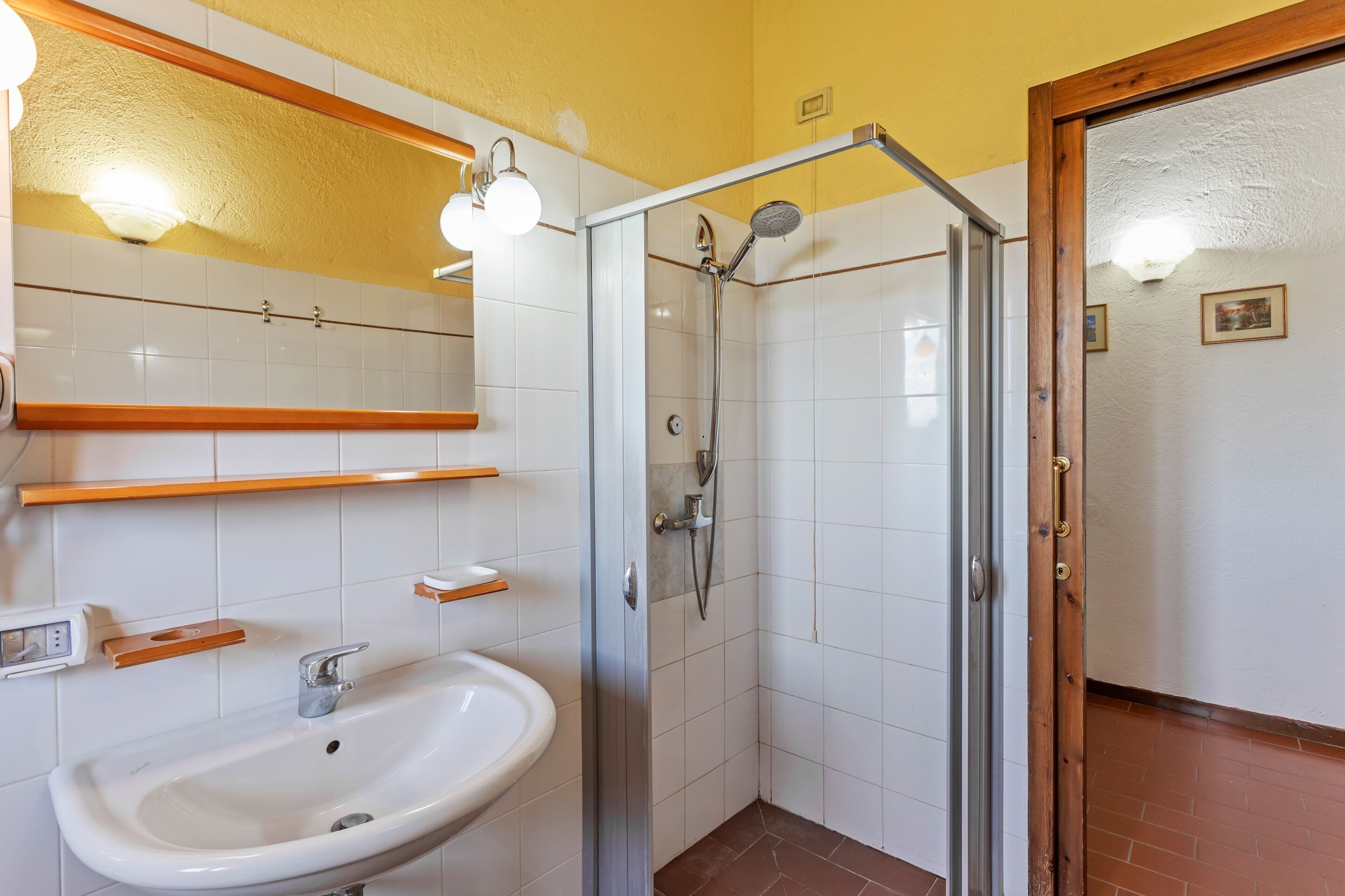A bathroom with a white sink, a glass shower enclosure, and a wooden door.