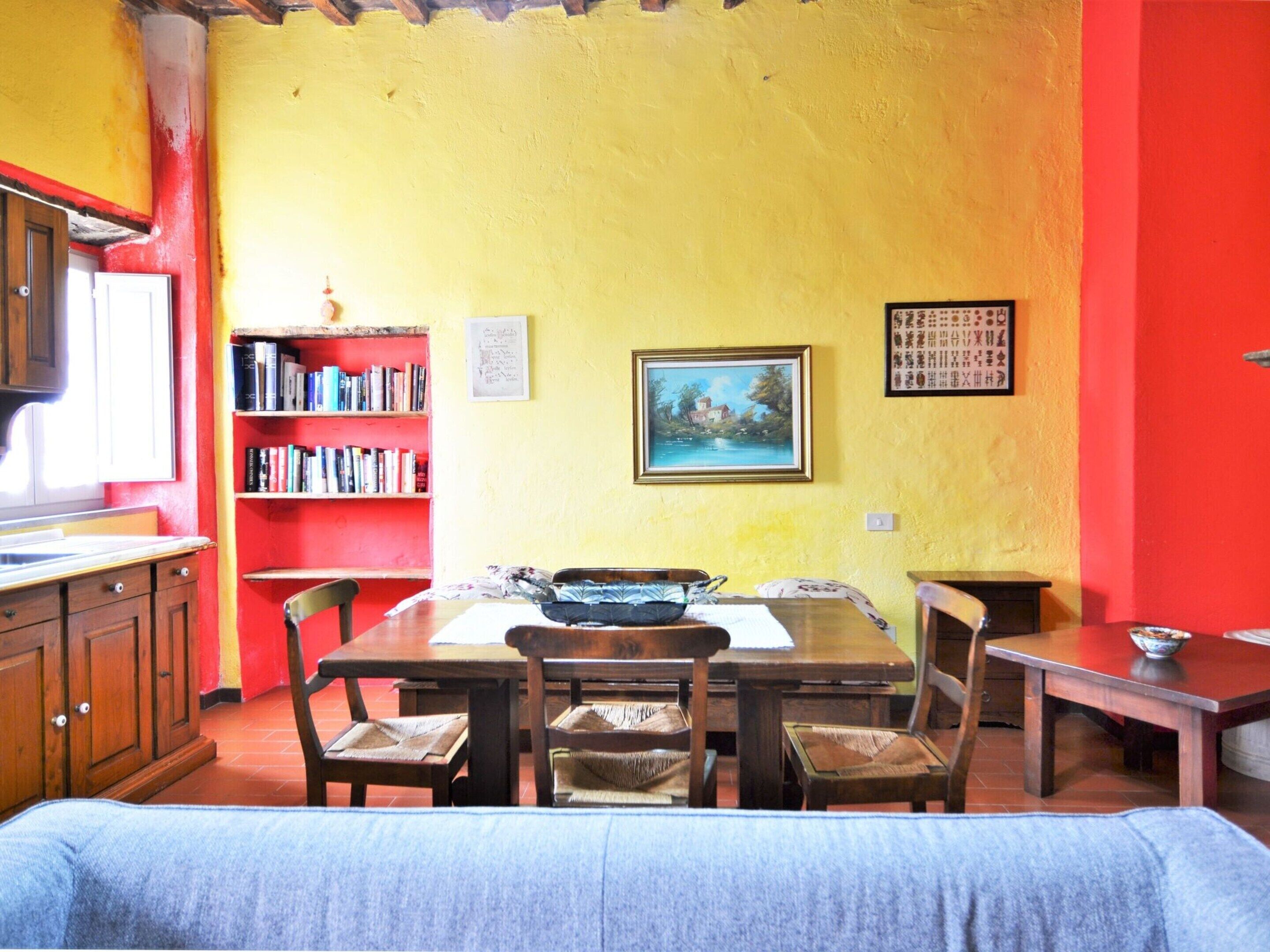 Comedor con mesa de madera, sillas y una estantería llena de libros.