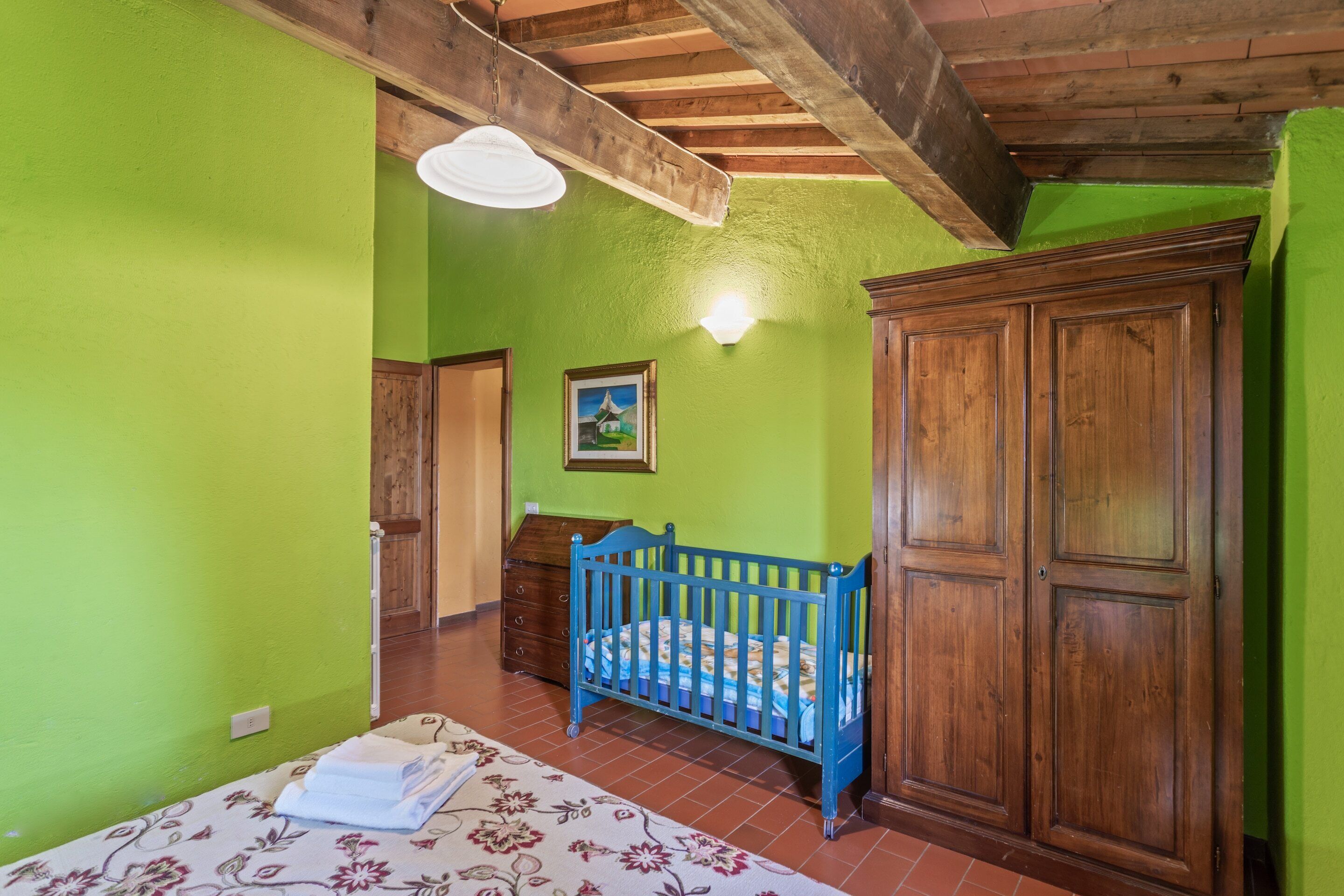 A room with green walls, a wooden ceiling, a crib, a wardrobe, and a bed with a floral bedspread.