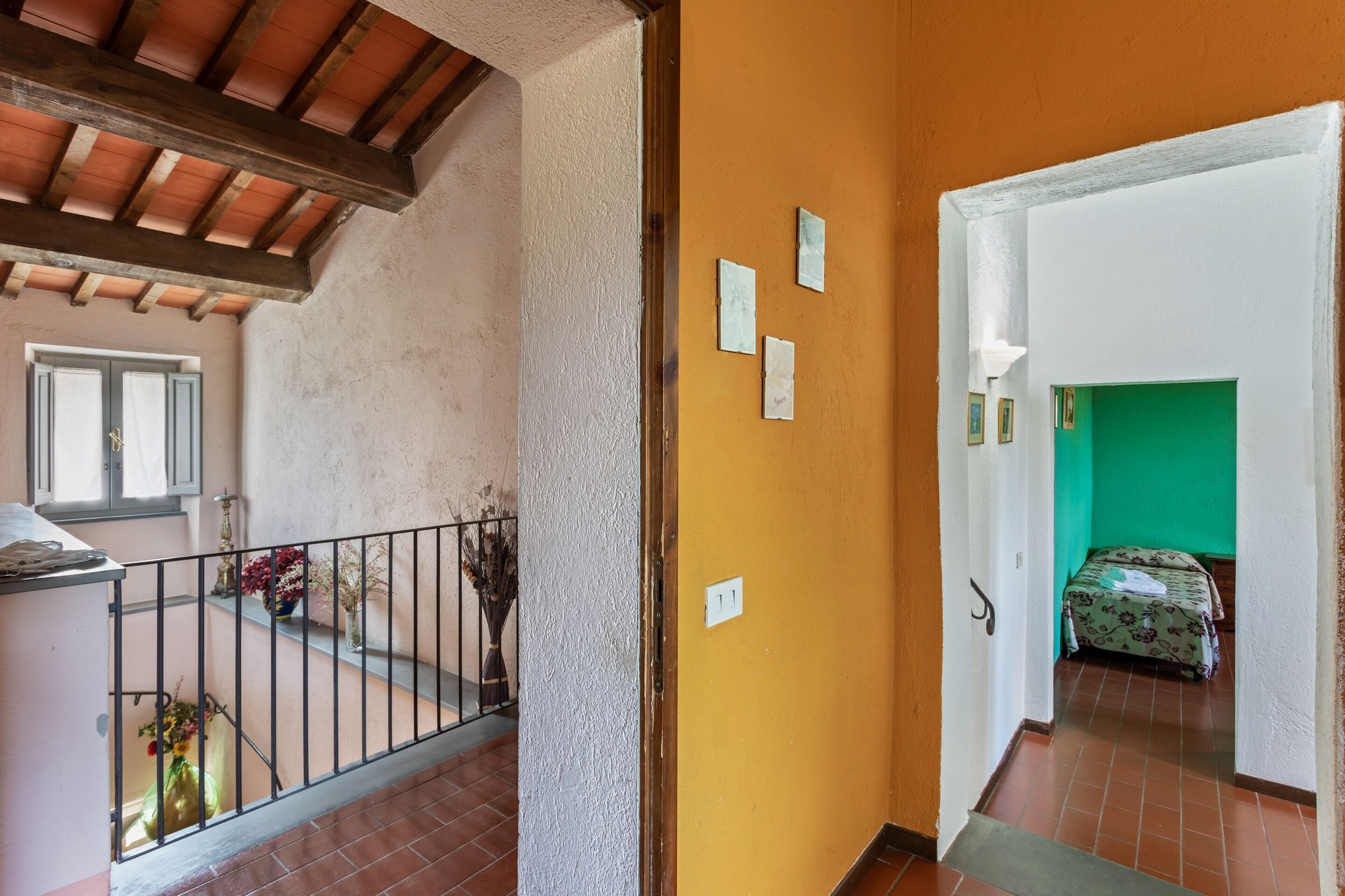 Un corridoio con una parete gialla, una stanza verde in lontananza e una scala con ringhiera.
