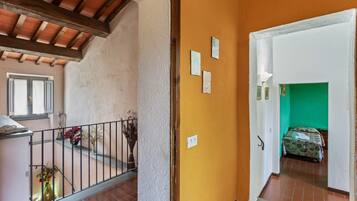 Un corridoio con una parete gialla, una stanza verde in lontananza e una scala con ringhiera.