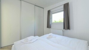 A bedroom with a bed, a window with curtains, and a radiator. - Brand new Chalets at 10 Minutes From the Oosterschelde (Heinkenszand)