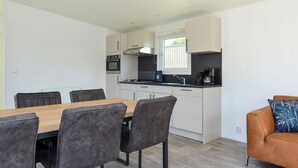 A modern kitchen with white cabinets, a black countertop, and a dining area with a wooden table and chairs. - Brand new Chalets at 10 Minutes From the Oosterschelde (Heinkenszand)