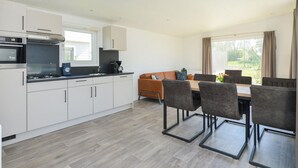 A modern kitchen with white cabinets, a built-in oven, and a dining area with a wooden table and chairs. - Brand new Chalets at 10 Minutes From the Oosterschelde (Heinkenszand)