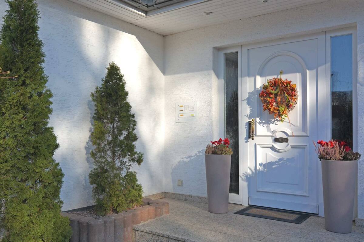 A white exterior wall with a door, two potted plants, and a small tree.