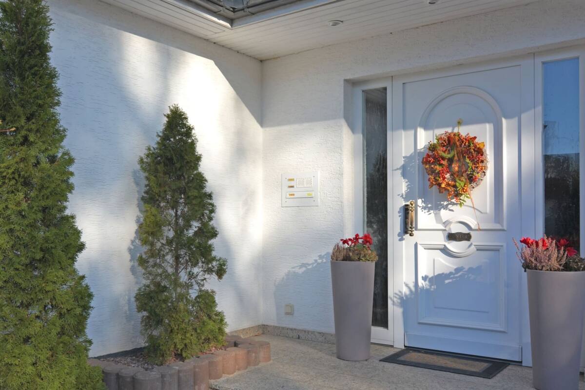 A white exterior wall with a door, a small tree, and two potted plants.