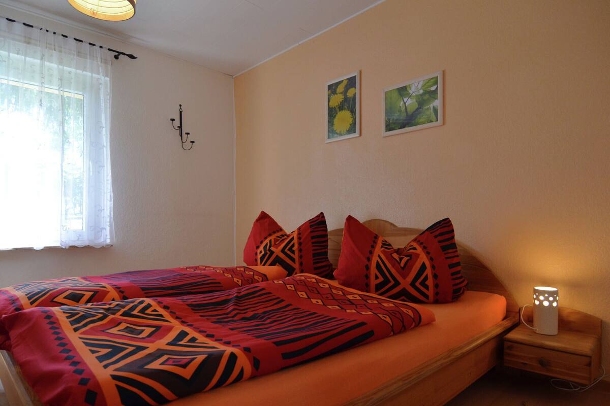 A bedroom with a bed, a nightstand, a lamp, and two wall-mounted pictures.