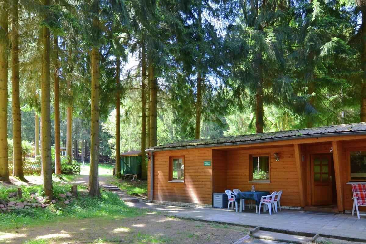A wooden cabin with a patio area, surrounded by tall trees.