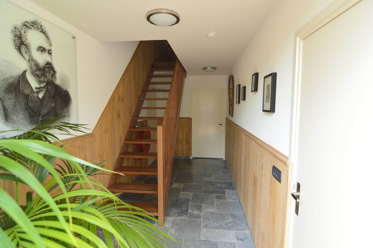 Un escalier avec des marches en bois menant à un palier, un tableau accroché au mur et une porte dotée d’une poignée.