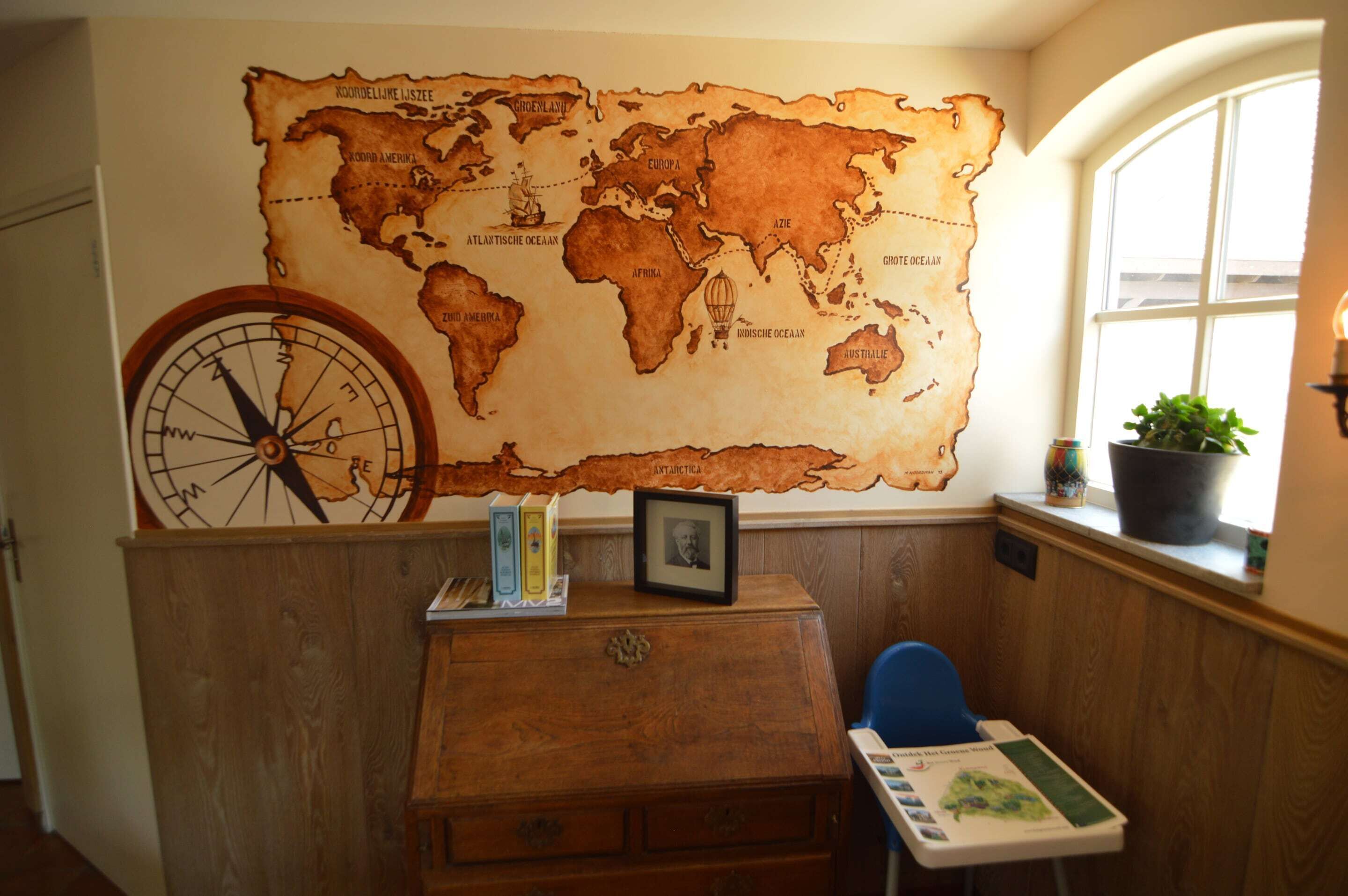 A room with a large world map on the wall, a wooden dresser, a blue chair, and a window with a view of the outdoors.