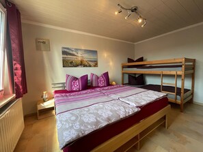 A bedroom with a bunk bed, a bed with patterned bedding, a bedside table with a lamp, and a ceiling light fixture. - Modern Bungalow in Warnkenhagen Near Wellness (Kalkhorst)