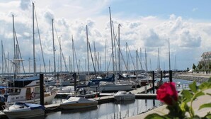 Un puerto deportivo con varias embarcaciones amarradas, cielo despejado y un edificio al fondo.