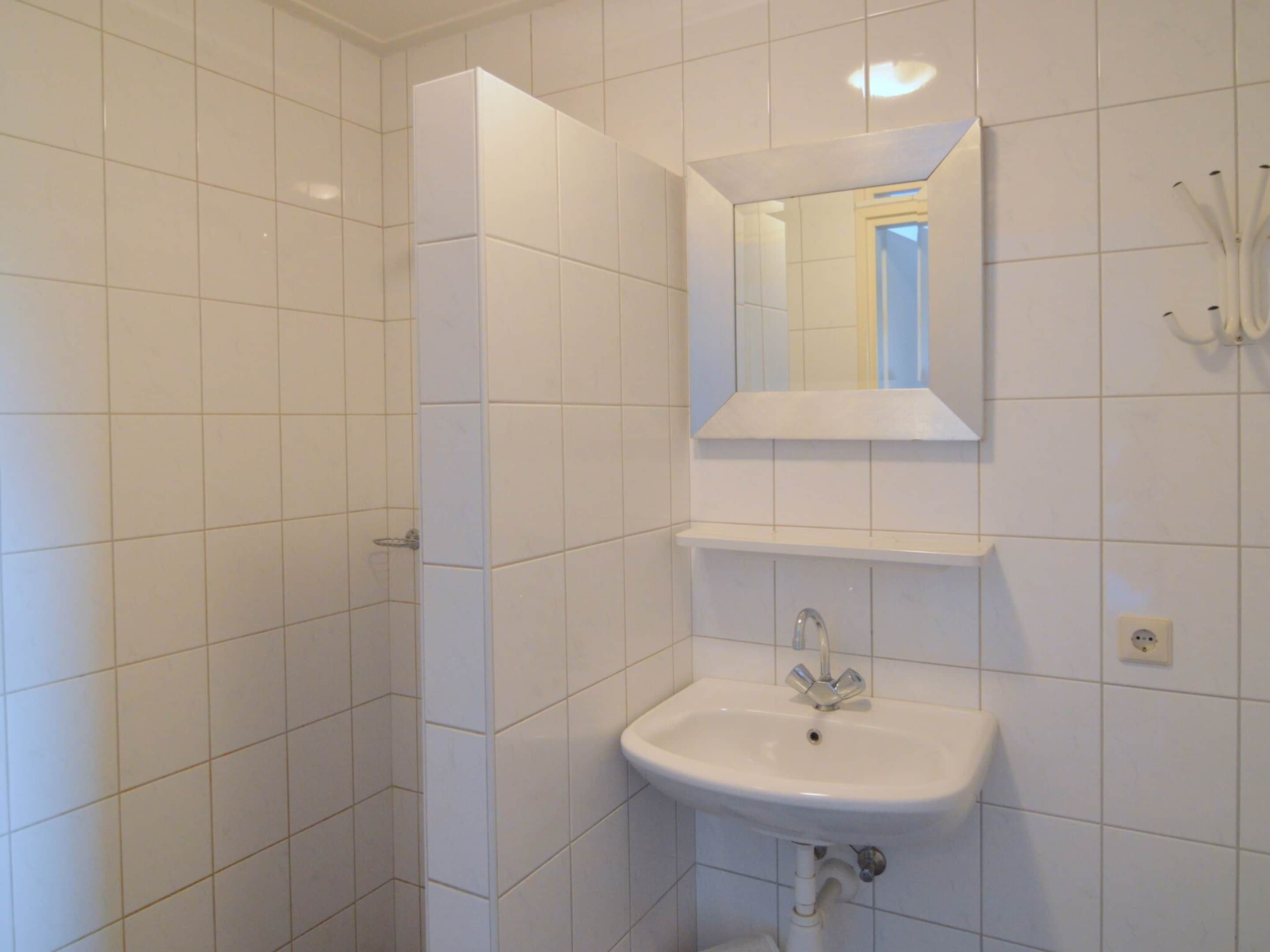 Ein Badezimmer mit weißen Fliesen, einem Waschbecken, einem Spiegel und einer Duschkabine.