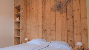 Une chambre avec une tête de lit en bois, deux tables de chevet avec des lampes, un lit avec une literie blanche et une décoration murale représentant un papillon.