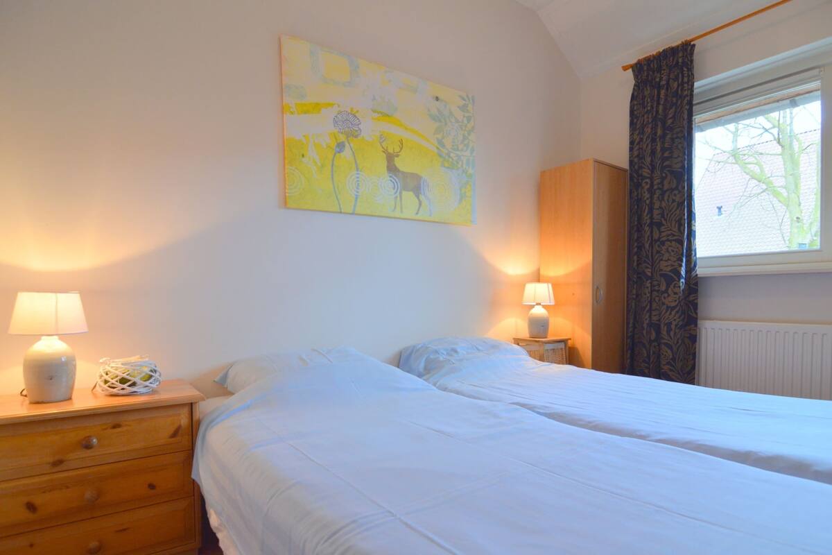 A bedroom with two beds, a wooden dresser, a lamp, and a painting on the wall.