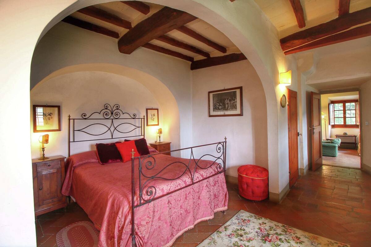 A bedroom with a metal bed frame, a red bedspread, and a wooden nightstand with a lamp.