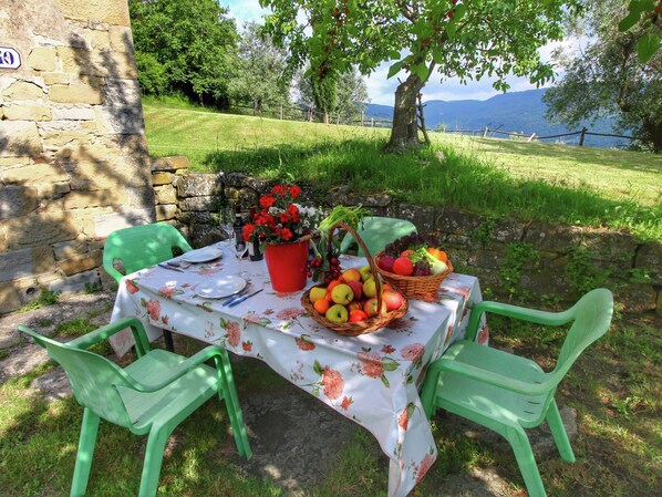 Un espace de restauration en plein air avec une table dressée pour deux personnes, entourée de murs en pierre et de verdure.