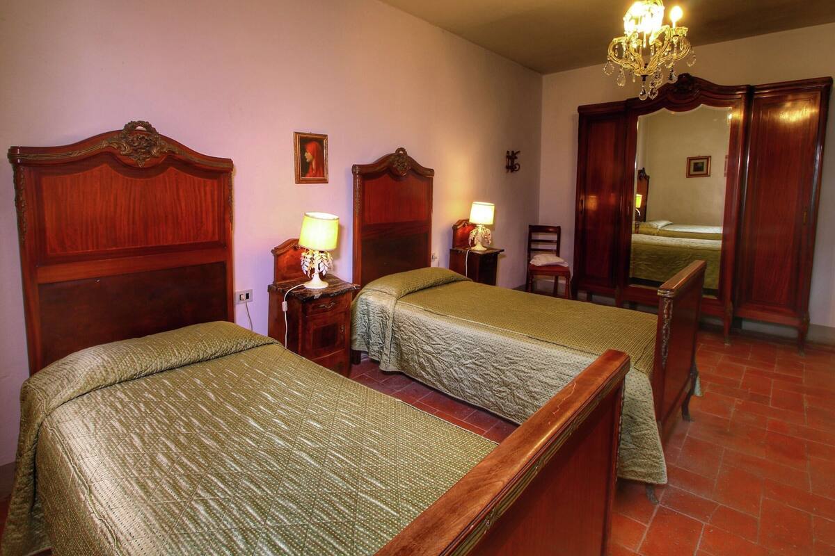 A hotel room with two beds, wooden headboards, a chandelier, a mirror, and a small table with a lamp.