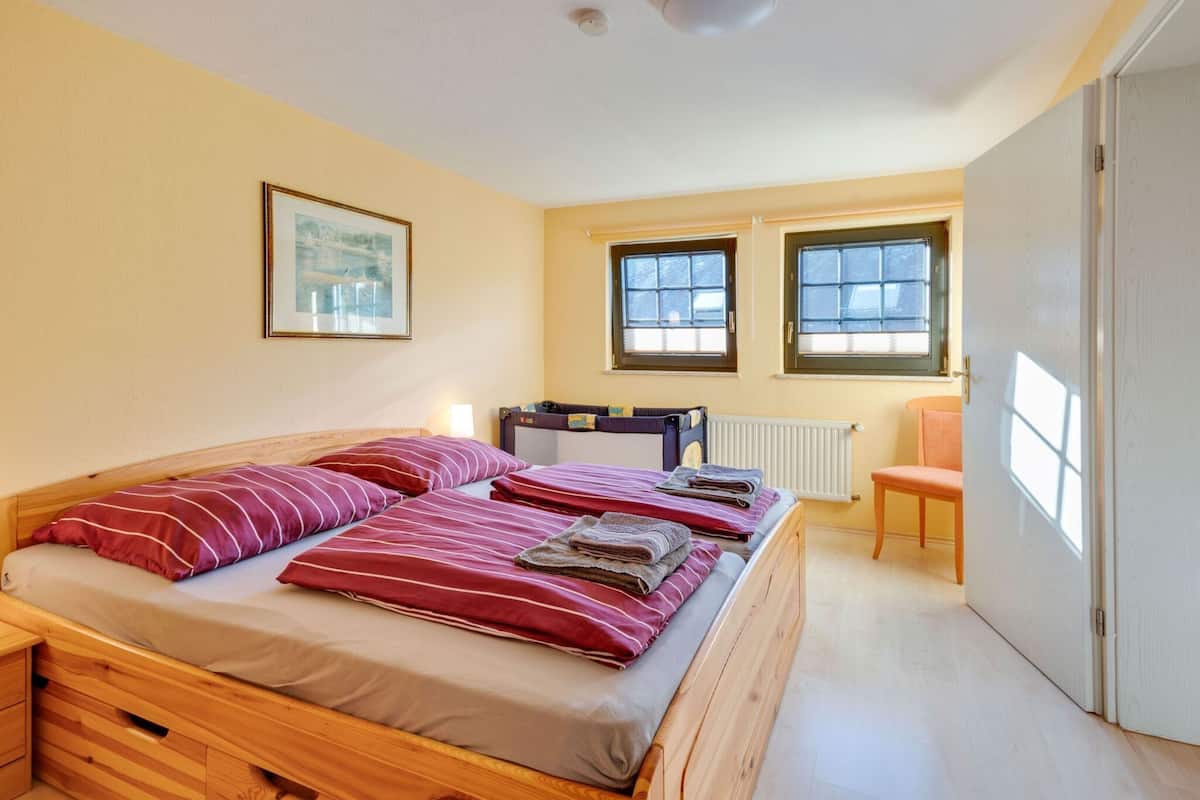 A bedroom with a wooden bed, two windows, a radiator, and a door.