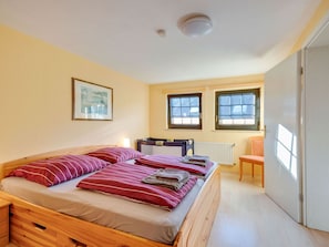 A bedroom with a wooden bed, two windows, a radiator, and a door.