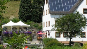 En bygning med sadeltag, solpaneler, en hvid facade og en stentrappe, der fører op til et rødt markise.
