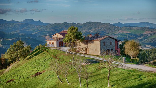 A stone house with a red roof on a hillside, surrounded by lush green hills and a clear sky. - Flat on a Farm With Swimming Pool and Many Activities (Sant'Angelo in Vado)