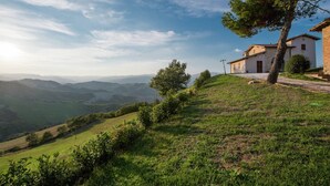 A hillside view with a stone building, a tree, and rolling hills in the background. - Flat on a Farm With Swimming Pool and Many Activities (Sant'Angelo in Vado)